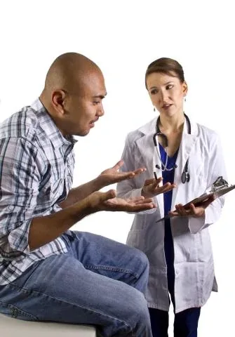 A doctor in a white coat with a clipboard listening to a seated patient