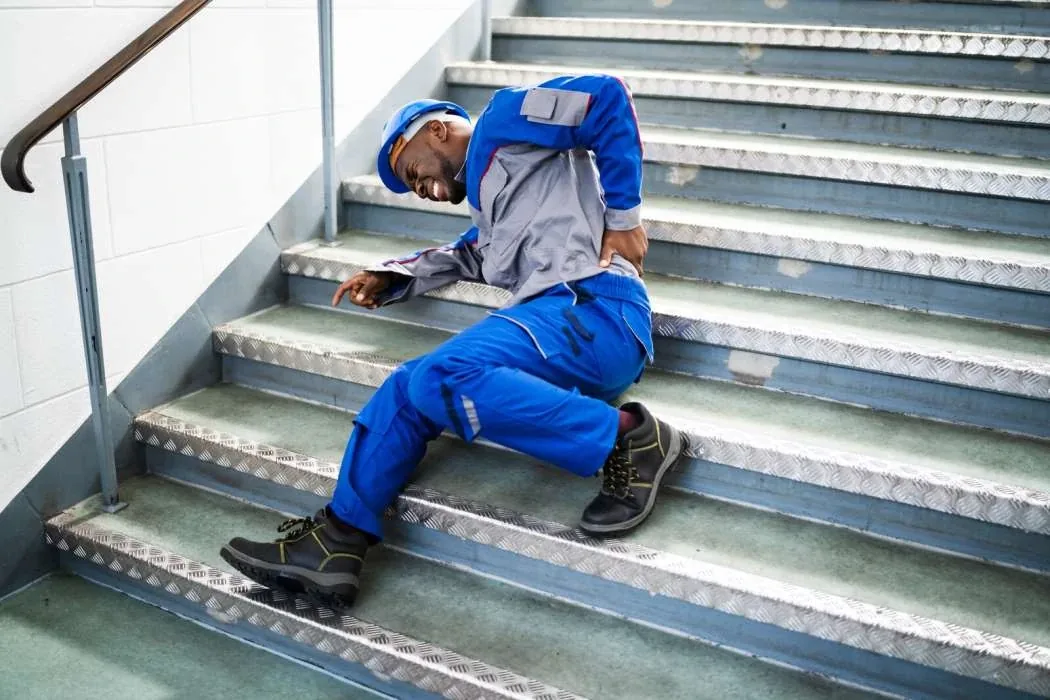 A worker in a hard hat holding his back after falling on a staircase